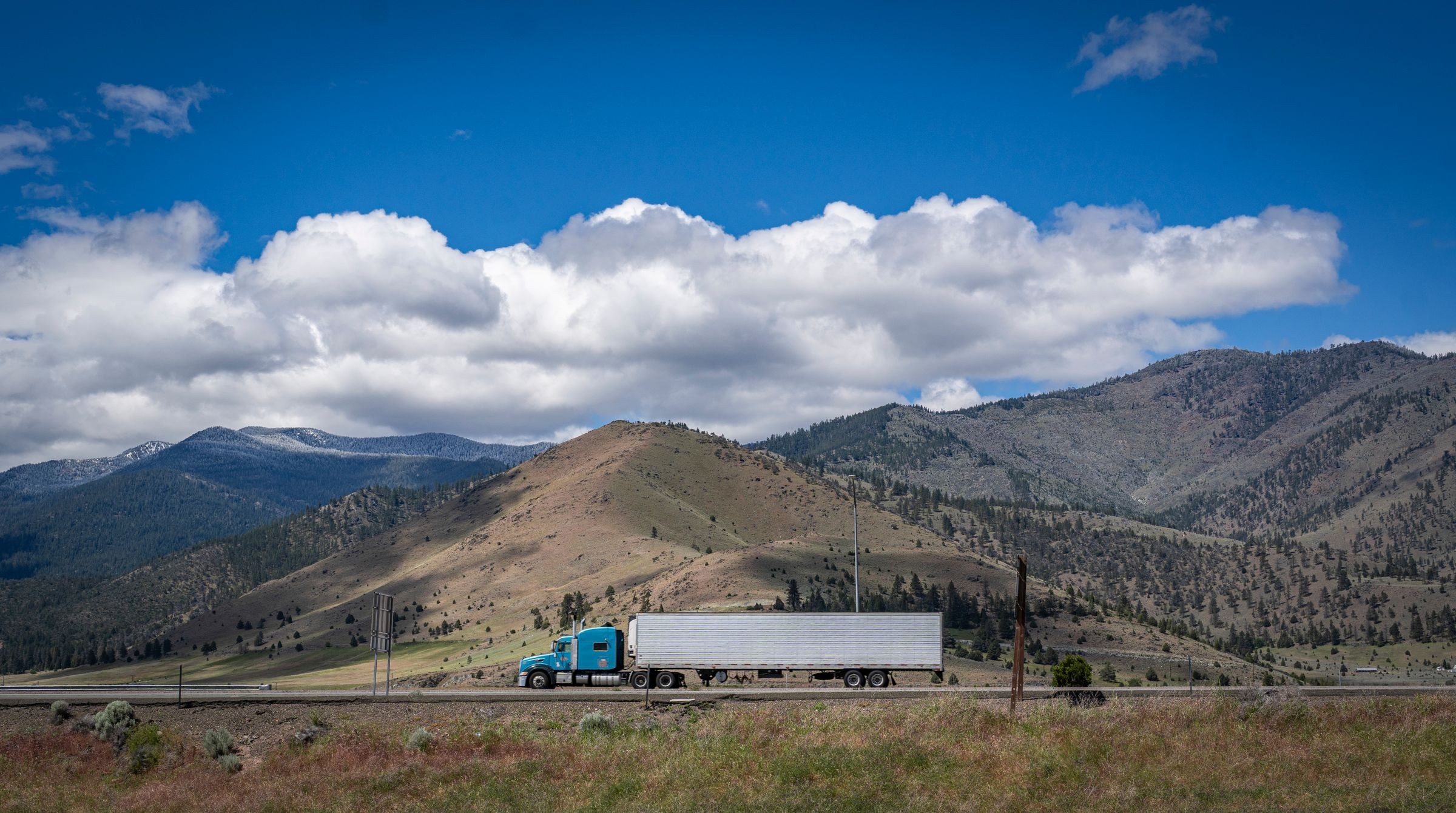 Blue semi-truck hauling a dry van trailer along a sunlit highway