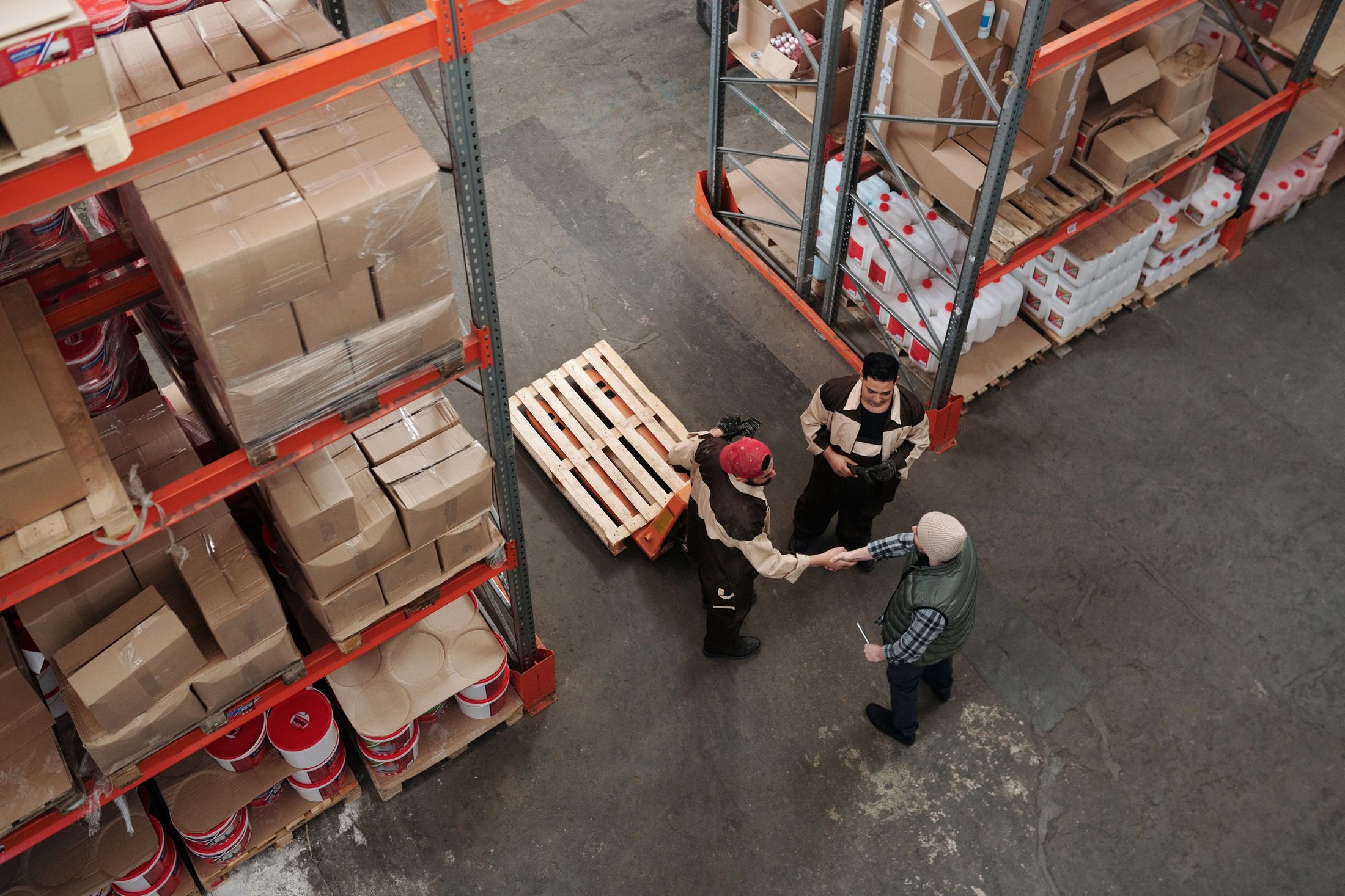 Warehouse workers meeting and shaking hands beside stored goods